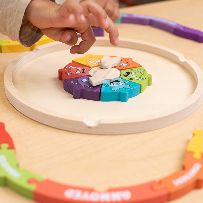 Child's hand interacting with a colorful toy on a wooden surface.